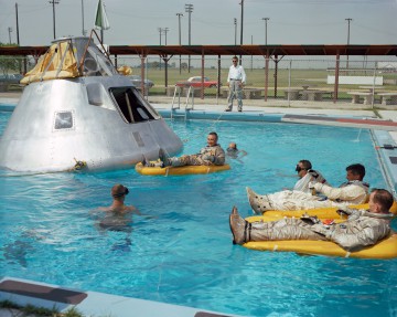 Ed White (foreground) and Roger Chaffee observe Gus Grissom (next to Apollo spacecraft mockup) during water egress exercises in June 1966. Photo Credit: NASA