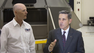Florida Gov. Rick Scott, left, listens as Robert Cabana, Kennedy Space Center director, details plans to assemble and process the Orion spacecraft in the Operations and Checkout Building at Kennedy. Behind them, an Orion test article stands in the high bay. Photo credit: NASA/Jim Grossmann