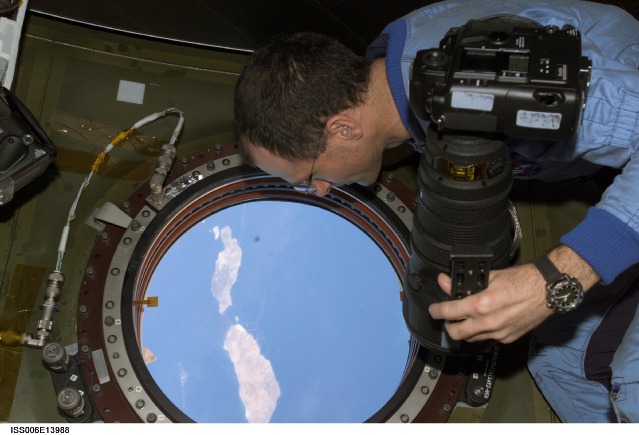 Don Pettit on the ISS during Expedition 6, holds a still camera as he looks through the nadir window in the Destiny laboratory on the International Space Station (ISS). The islands of Lanzarote and Fuerteventura of the Canary Island chain in the Atlantic Ocean off the coast of Morocco are visible. Photo Credit: NASA