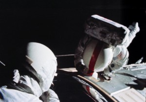 Wearing John Young's red-striped helmet, Ken Mattingly works outside the service module during his Deep-Space EVA. Nearby, Charlie Duke assists from the command module's hatch. Photo Credit: NASA