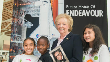 Lynda Oschin with students from the Science Center School. Students unfurled a banner displaying newly named Samuel Oschin Air and Space Center, future permanent home of the Space Shuttle Endeavour. Photo Credit: Leroy Hamilton (used with permission)