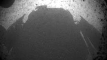 One of the first images from Curiosity after landing on the surface of Mars, clearing showing a flat surface with the rover's shadow cast by the mid-afternoon sun. Photo Credit: NASA/JPL-Caltech