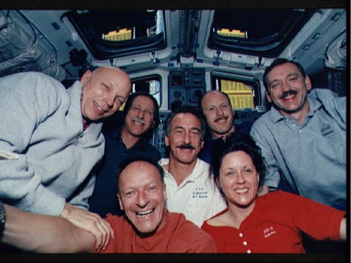 Backdropped by the Hubble Space Telescope through Endeavour's aft flight deck and overhead windows, the STS-61 crew celebrates their success. On the front row are Claude Nicollier and Kathy Thornton, with Story Musgrave, Dick Covey, Jeff Hoffman, Ken Bowersox and Tom Akers behind. Photo Credit: NASA