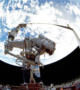 Laden with tools and equipment, Jeff Hoffman waves from the end of the RMS arm during Hubble repair operations. Photo Credit: NASA