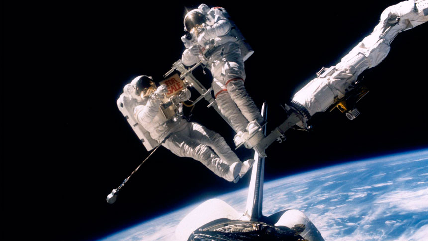 Joe Allen (right, with red stripes on the legs of his suit) and Dale Gardner celebrate their success with a "For Sale" sign, displayed high above Westar and Earth. Photo Credit: NASA