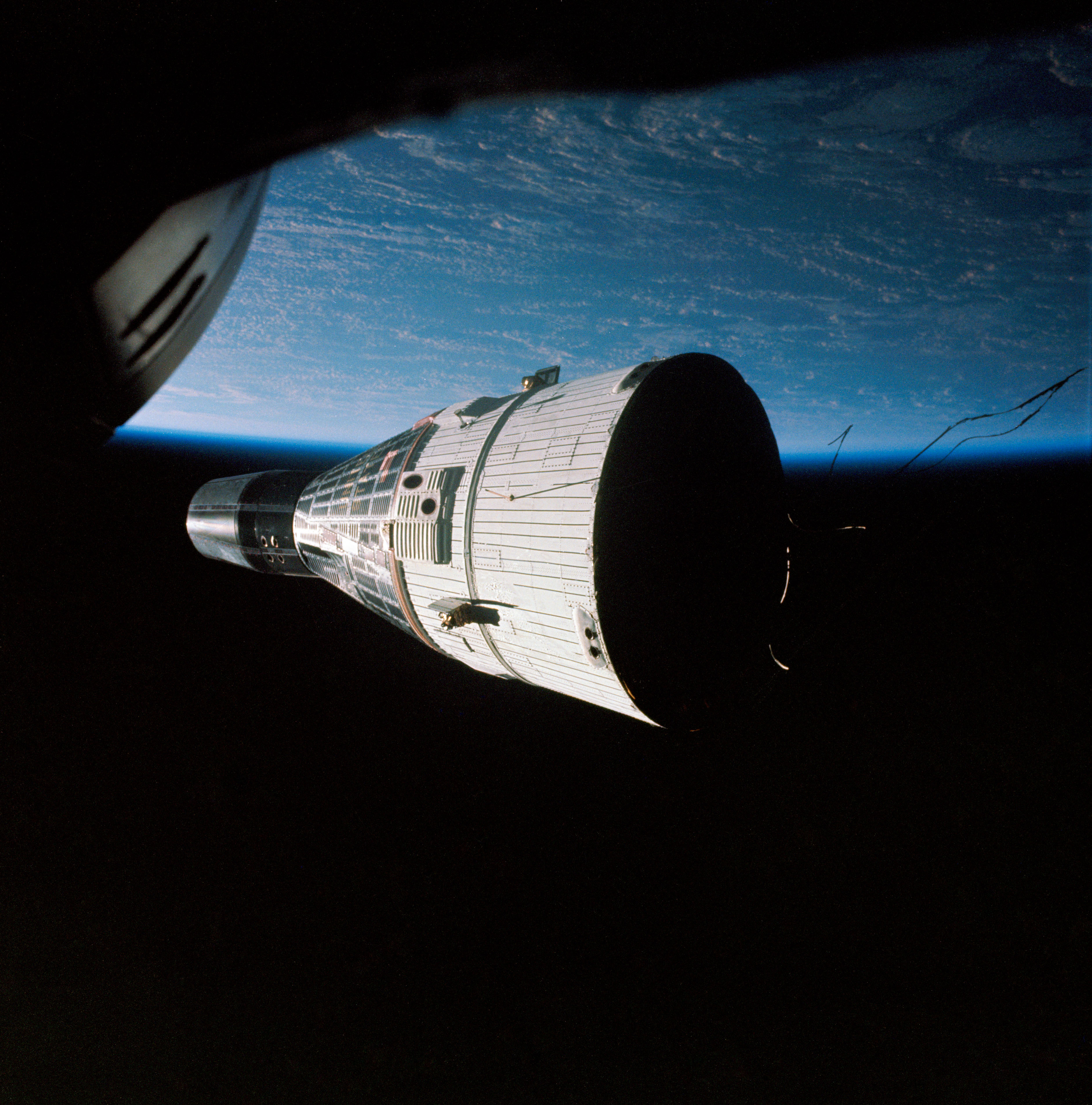 Backdropped by the grandeur of Earth, Gemini VII drifts serenely in the inky darkness, as seen from Gemini VI-A. Photo Credit: NASA