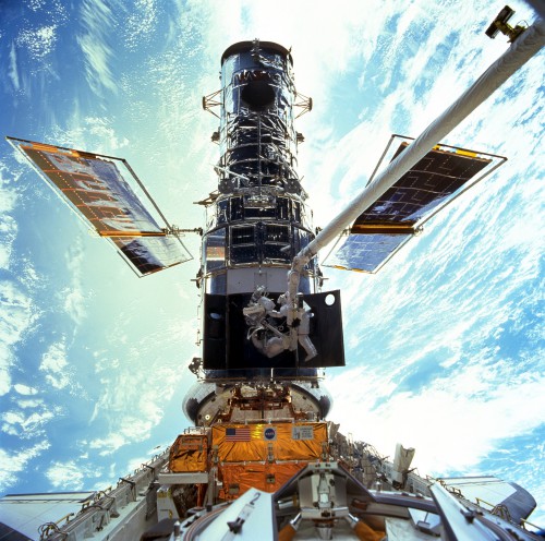 Hubble being serviced by astronauts from the space shuttle Discovery on mission STS-103 in December 1999. Astronauts Steven L. Smith, and John M. Grunsfeld, appear as small figures in this wide scene photographed during a space walk to replace Hubble's gyroscopes. Photo Credit: NASA