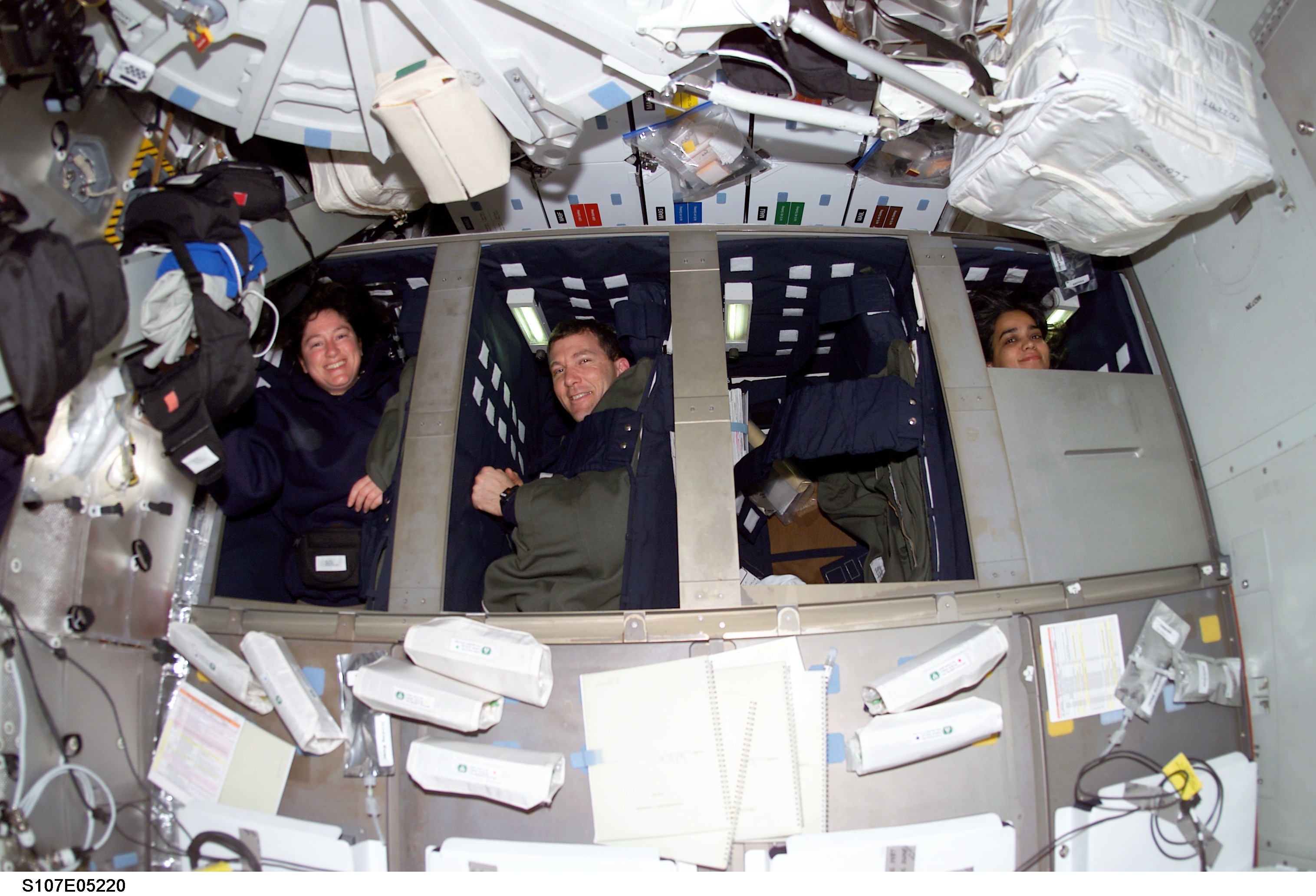 The dual-shift nature of STS-107 required the inclusion of sleep stations in Columbia's middeck. In this image, Red Team members Laurel Clark, Rick Husband and Kalpana Chawla peek out of their bunks. Photo Credit: NASA