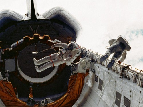 Story Musgrave (left) and Don Peterson perform the Shuttle program's first EVA. The large tilt-table, used earlier in the mission to deploy the first Tracking and Data Relay Satellite, is visible in the background. Photo Credit: NASA