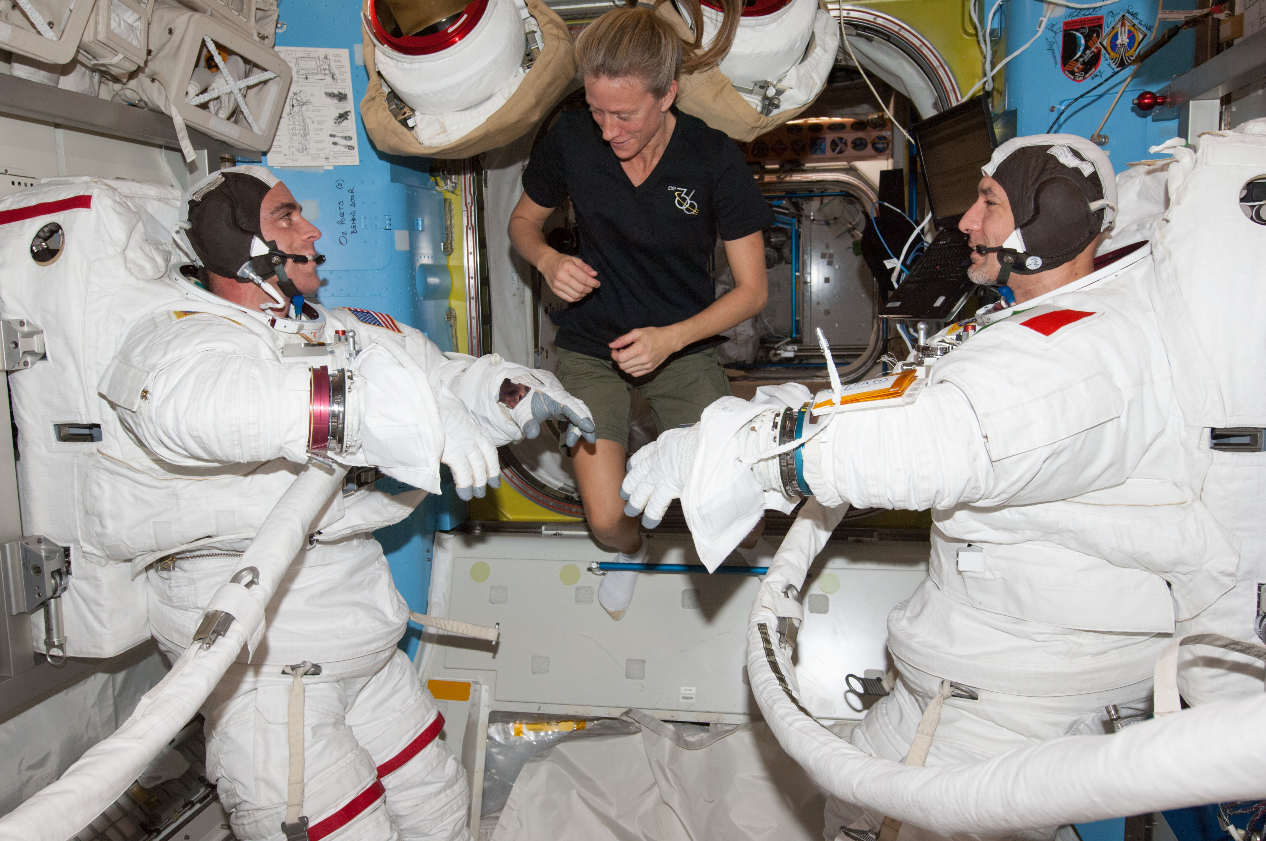 Karen Nyberg (center) assists EVA crewmates Chris Cassidy (left) and Luca Parmitano in the Quest airlock, during a "dry run" of their suit-up procedures on Wednesday 3 July. Photo Credit: NASA