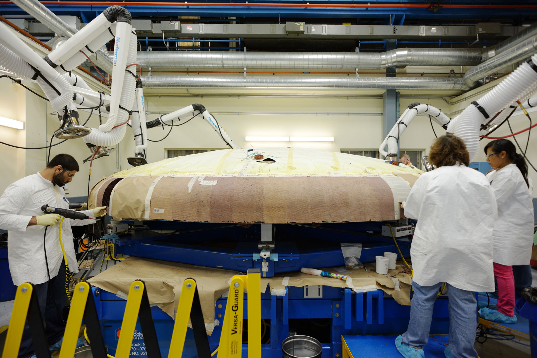 A team of technicians at Textron Defense Systems apply Avcoat ablative material to the composite honeycomb structure attached to the Orion heat shield carrier structure. The ablative material is designed to protect the spacecraft from extreme temperatures during re-entry. Image Credit: NASA