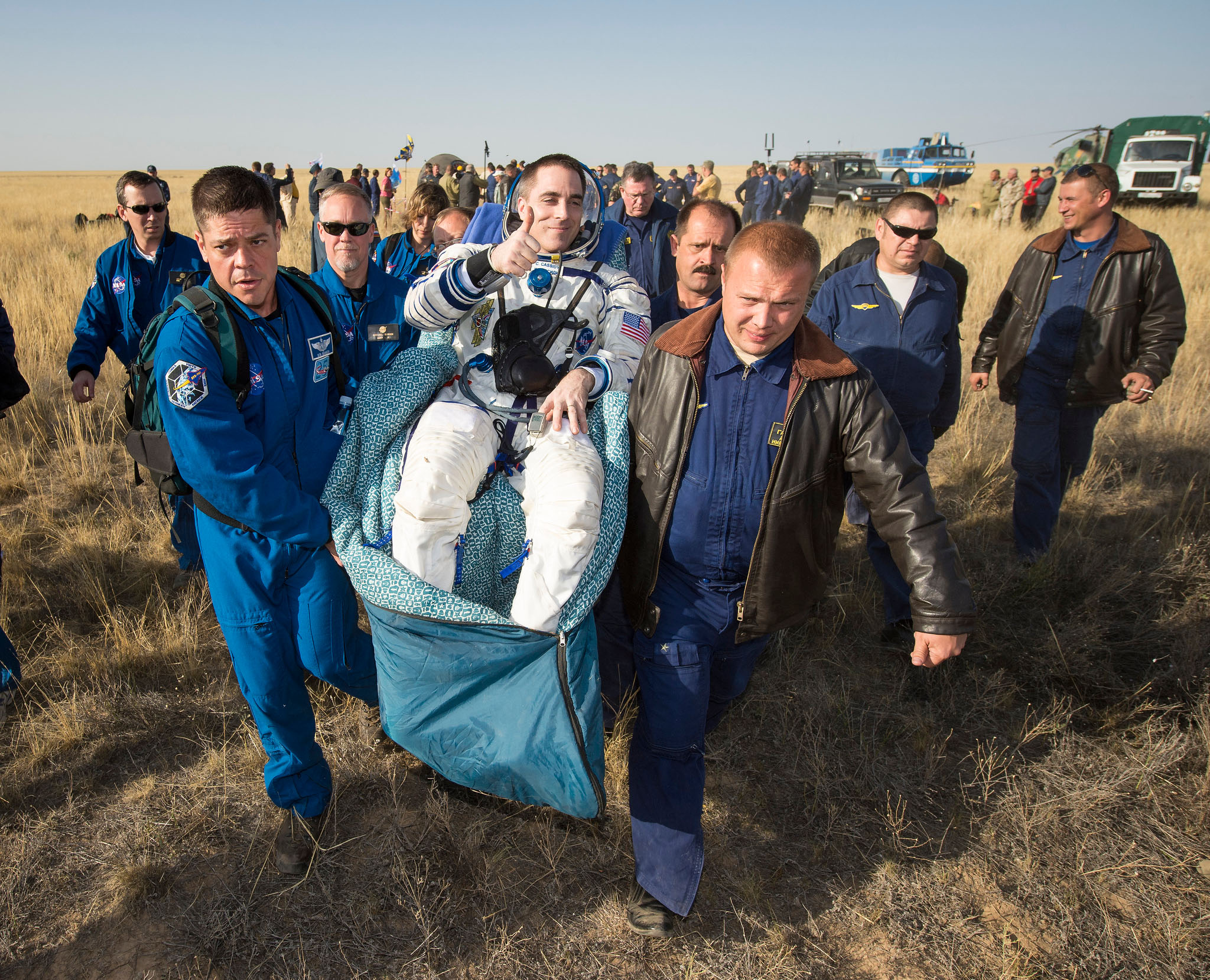 Helped by support personnel, including Chief Astronaut Bob Benken (left), Soyuz TMA-08M crewman Chris Cassidy gives a thumbs-up after his return from a 166-day space mission. Photo Credit: NASA