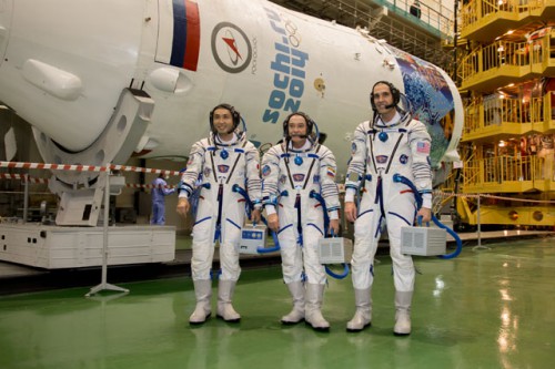 Backdropped by their rocket's payload shroud and its Sochi Olympics mural, Soyuz TMA-11M crewmen (from left) Koichi Wakata, Mikhail Tyurin and Rick Mastracchio are pictured in their Sokol launch and entry suits at Baikonur. Photo Credit: NASA