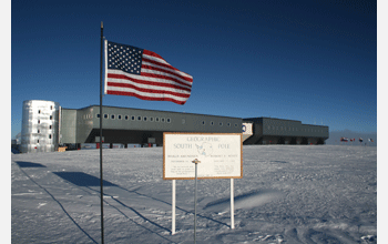 The Amundsen-Scott South Pole Station building in the backgroung. The sign and brass pole next to the US flag in the forground, mark the exact point of the geographic South Pole. Image Credit: Ethan Dicks, National Science Foundation.