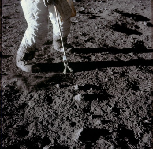 The lower legs of his space suit blackened by lunar dust, Pete Conrad uses the tongs of an Apollo Lunar Hand Tool to gather a rock sample at the Ocean of Storms. Photo Credit: NASA