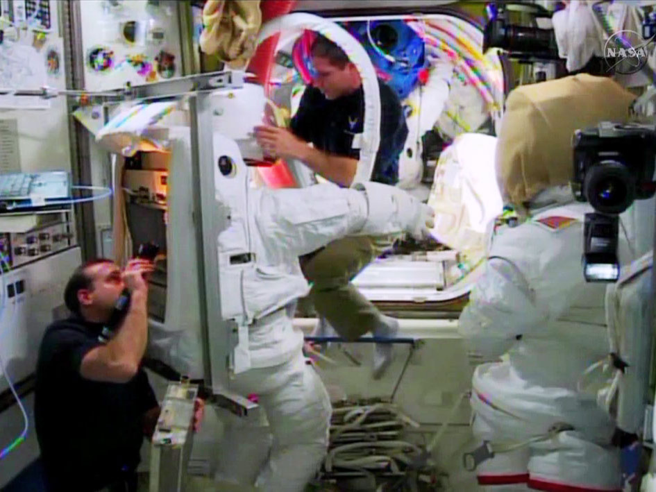 Expedition 38 astronauts Rick Mastracchio (bottom left) and Mike Hopkins (top right) work with their space suits inside the Quest airlock, as preparations for the Christmas EVAs gather momentum. Photo Credit: NASA