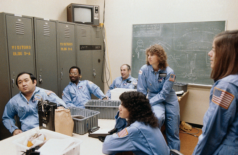 Members of the 51L crew during training. From left are Ellison Onizuka, Ron McNair, Greg Jarvis, Judy Resnik, Christa McAuliffe (seated on table) and backup crew member Barbara Morgan. Photo Credit: NASA