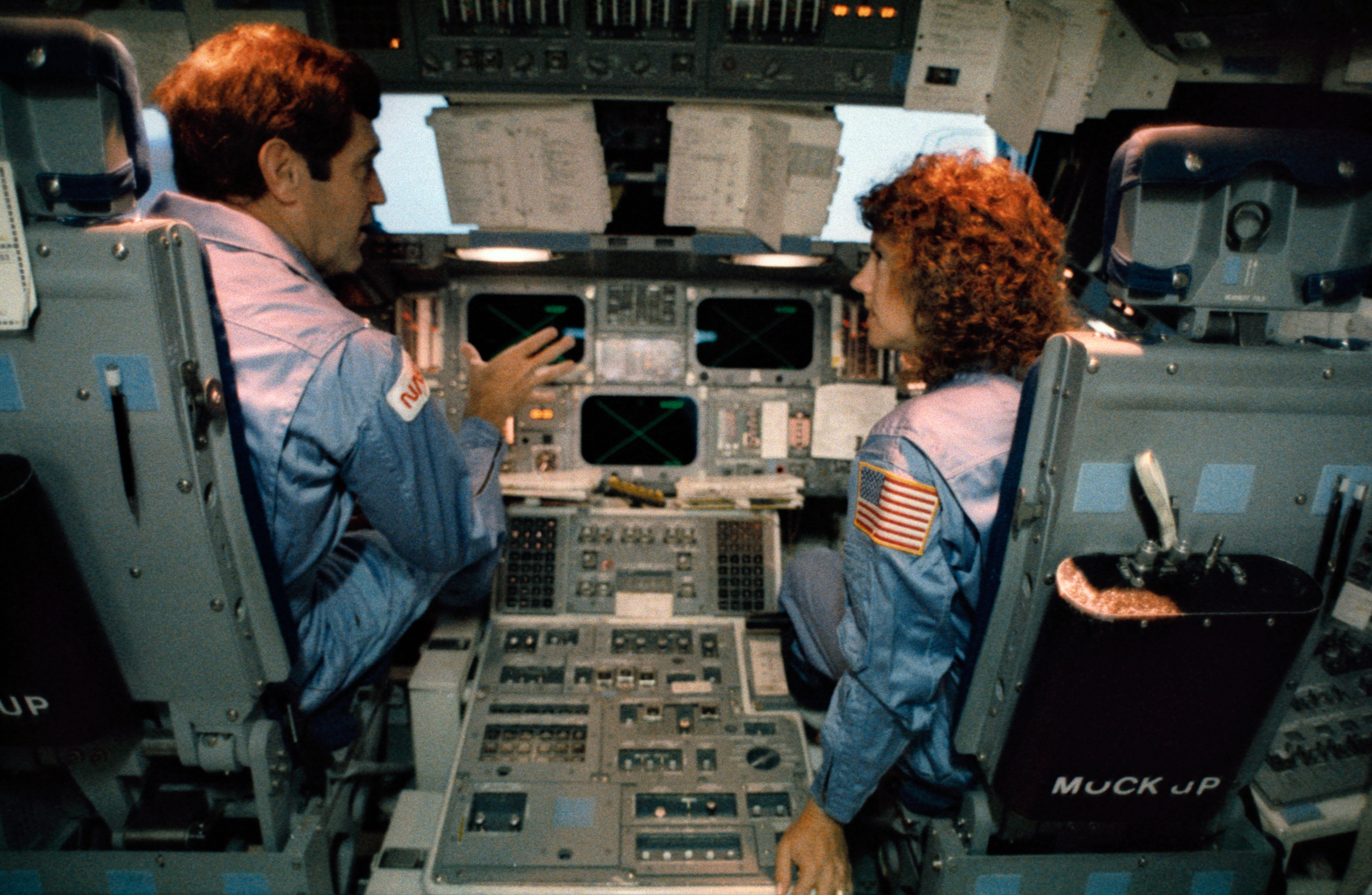 Mission 51L Commander Dick Scobee talks to schoolteacher Christa McAuliffe about the instrumentation of the shuttle's flight deck during pre-launch training. Photo Credit: NASA