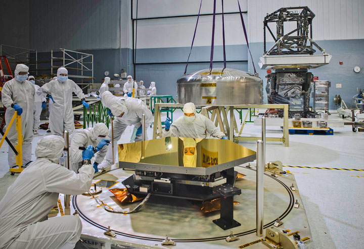 The amazing mirrors that will fly aboard NASA's James Webb Space Telescope will allow the James Webb Space Telescope to see farther away and further back in time to detect the light from the very first and most distant stars and galaxies. In this photo, an engineer's crystal clear reflection is seen on the surface of one of the primary mirror segments. The image is so clear you can see an expression of concentration in the engineer's face. Behind the engineer looking into the mirror's surface, the top part of the canister that the mirror was shipped in hangs from four straps. Other engineers use flashlights to inspect the mirror segment. Photo Credit and Caption: NASA/Chris Gunn