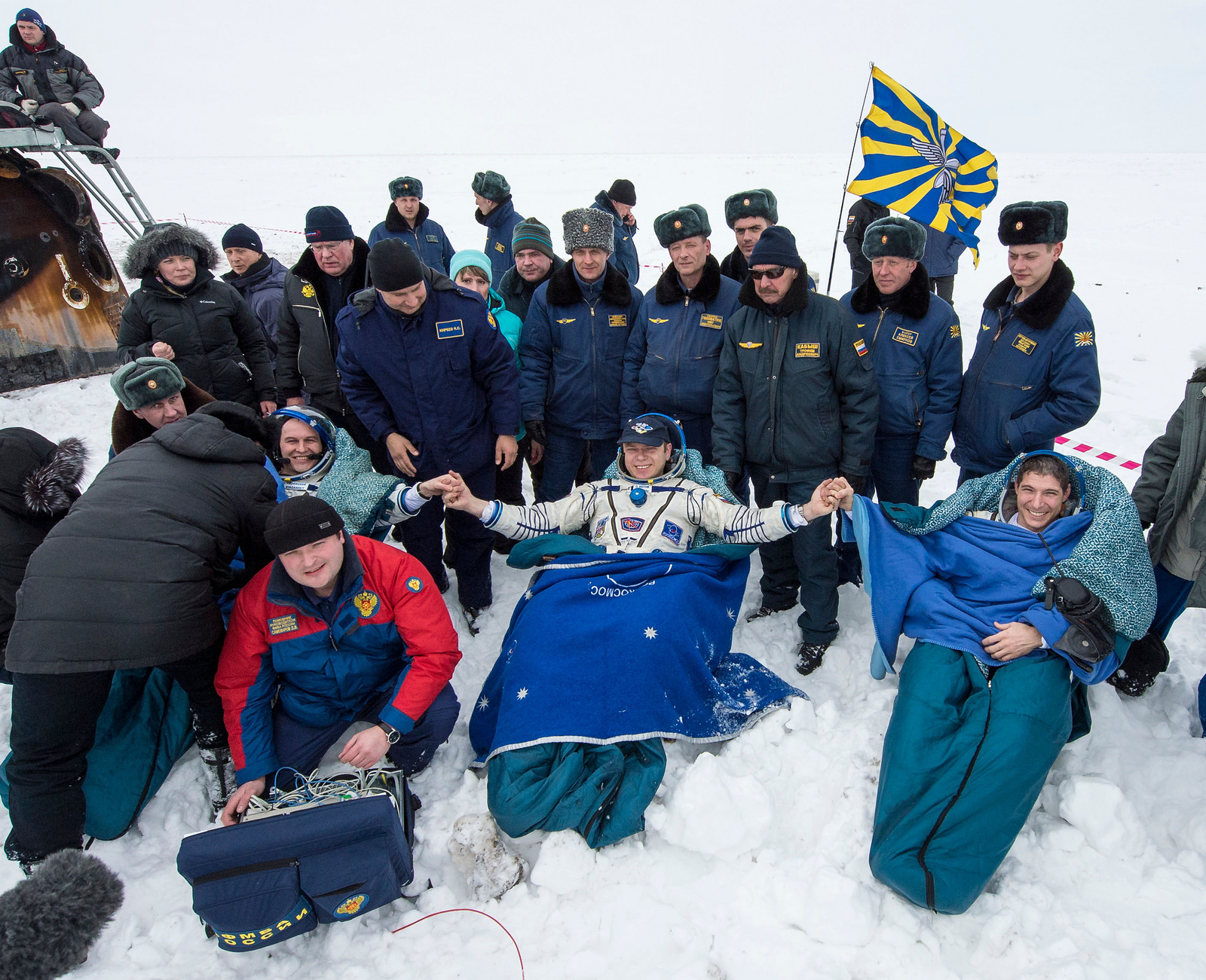 At the snowy landing site, not from the Kazakh city of Jezkazgan, Soyuz TMA-10M crewmen Oleg Kotov (center), Sergei Ryazansky (left) and Mike Hopkins (right) clasp hands in a sign of solidarity and recognition of a mission well done. Photo Credit: NASA