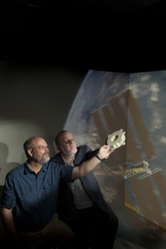 Goddard technologists Ted Swanson and Matthew Showalter hold a 3D-printed battery-mounting plate developed specifically for a sounding-rocket mission. The component is the first additive-manufactured device Goddard has flown in space. Image Credit/Caption: NASA/Goddard Space Flight Center