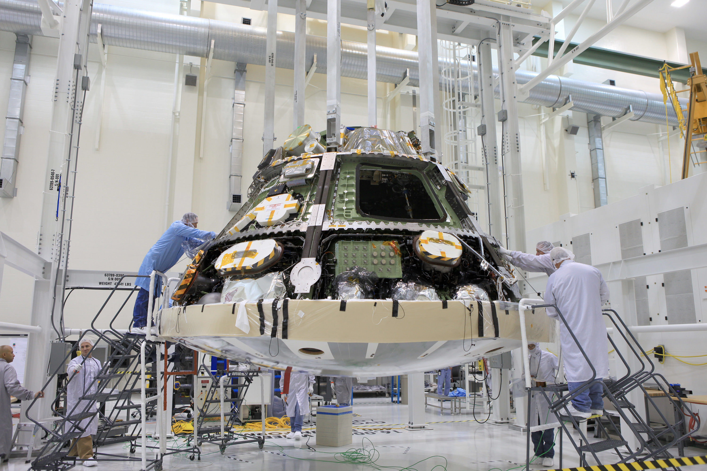 Lockheed Martin technicians and engineers attach the heat shield to the Orion crew module inside the Operations and Checkout Building high bay at NASA's Kennedy Space Center in Florida. Technicians have installed more than 200 instrumentation sensors on the heat shield for Exploration Flight Test-1, or EFT-1. The flight test will provide engineers with data about the heat shield's ability to protect Orion and its future crews from the 4,000-degree heat of reentry and an ocean splashdown following the spacecraft’s 20,000-mph reentry from space. Photo Credit: NASA / Daniel Casper