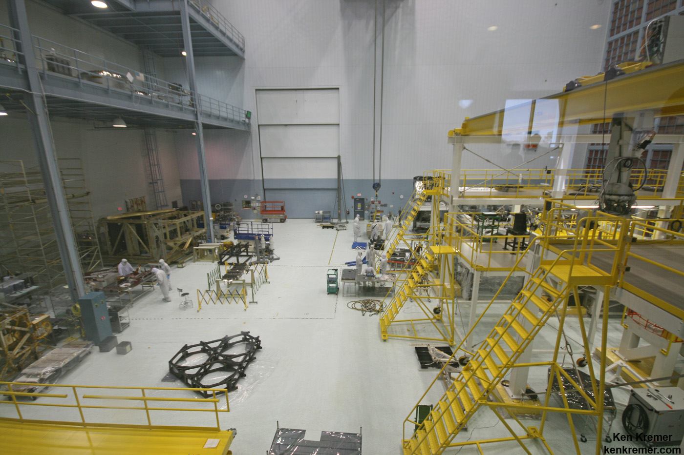 JWST is being assembled here inside the world’s largest clean room at NASA Goddard Space Flight Center, Greenbelt, Md. Primary mirror segments stored in silver colored containers at top left. Technicians practice mirror installation on test piece of backplane (known as the BSTA or Backplane Stability Test Article) at center, 3 hexagonals.  Telescope assembly bays at right.  Credit: Ken Kremer- kenkremer.com