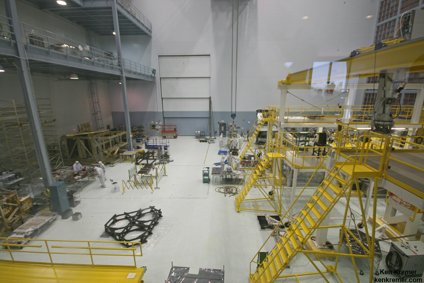 JWST is being assembled here inside the world’s largest clean room at NASA Goddard Space Flight Center, Greenbelt, Md. Primary mirror segments stored in silver colored containers at top left. Technicians practice mirror installation on test piece of backplane (known as the BSTA or Backplane Stability Test Article) at center, 3 hexagonals. Telescope assembly bays at right. Credit: Ken Kremer- kenkremer.com