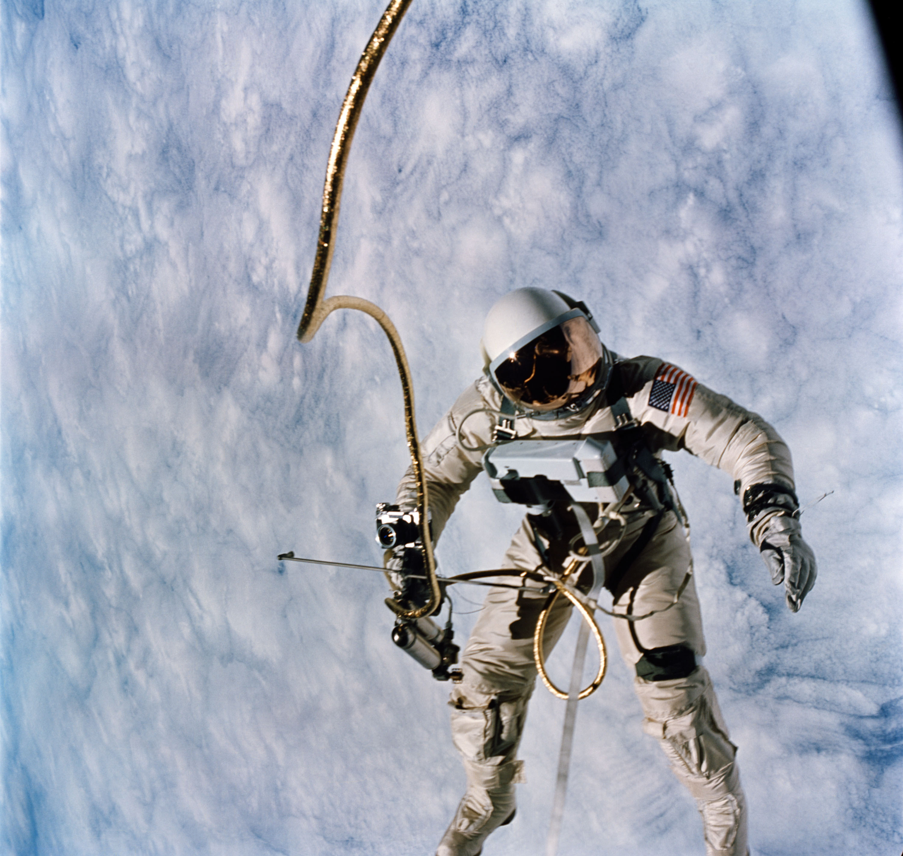 Clasping the cold-gas maneuvering gun in his right hand, and trailed by a snake-like tether, Ed White tumbles over a cloud-speckled Earth during the United States' first EVA. Photo Credit: NASA