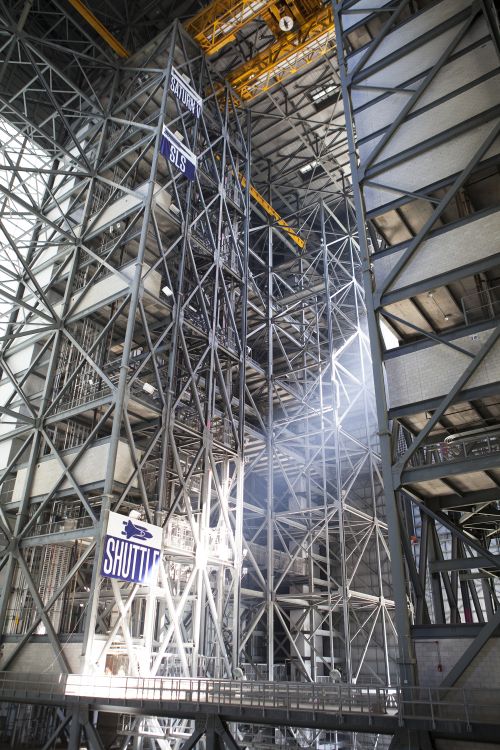 Steel structures surround High Bay 3 inside the Vehicle Assembly Building, or VAB, at NASA’s Kennedy Space Center in Florida. In view, high above, is the 175-ton crane. Banners note the heights of the Saturn V, Space Launch System, or SLS, and shuttle on the steel structure. Photo Credit: NASA/Dimitri Gerondidakis