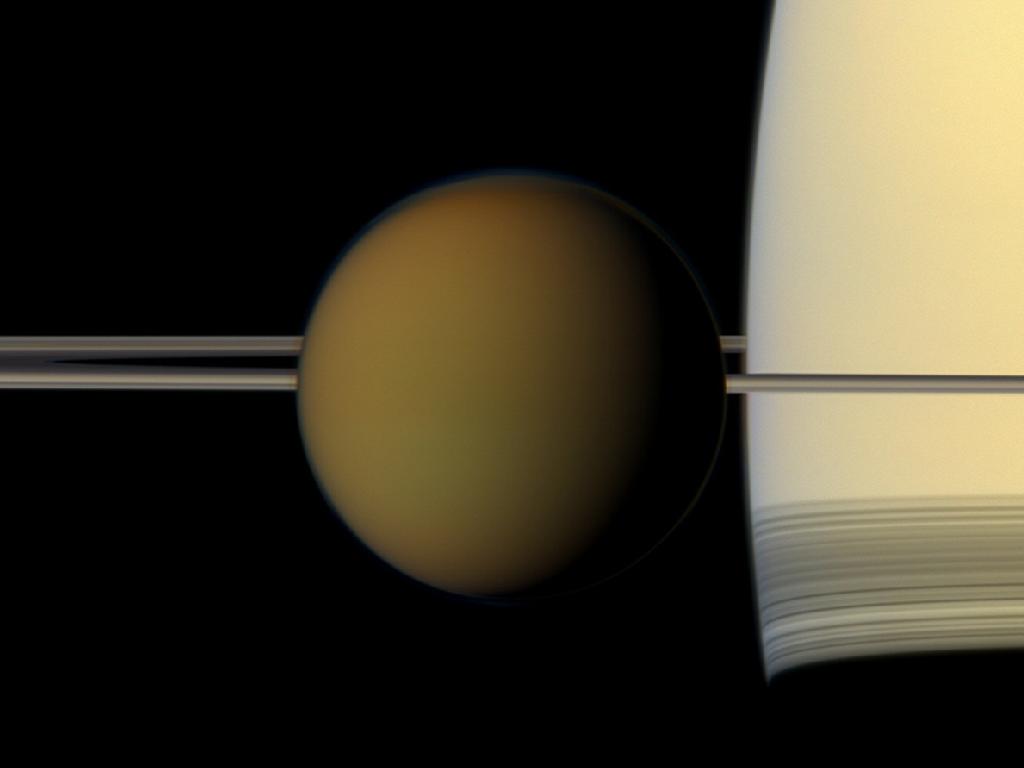 Titan's colorful globe passes in front of Saturn and its rings, in this true color image taken in 2011 from NASA's Cassini spacecraft. The moon's opaque atmosphere hides a fascinating surface that is rich in methane lakes, water ice and organic compounds. Image Credit: NASA/JPL-Caltech/Space Science Institute