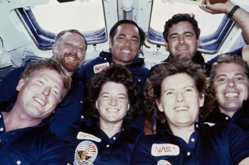 The crew poses for an in-flight photograph aboard Challenger. In the front row (from left) are Jon McBride, Sally Ride, Kathy Sullivan and Dave Leestma, with (from left) Paul Scully-Power, Bob Crippen and Marc Garneau behind. Photo Credit: NASA