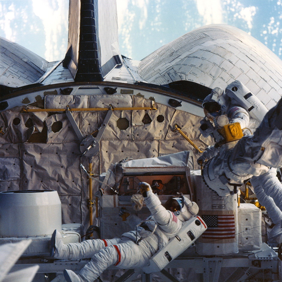 Dave Leestma (with red stripes on the legs of his suit) and Kathy Sullivan work on the refuelling experiment during their historic EVA. Photo Credit: NASA