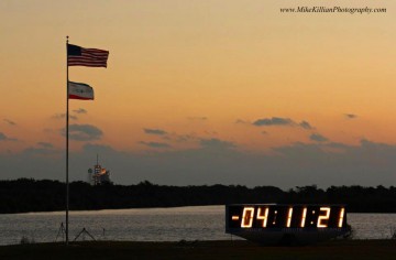 Sunrise approaches over the KSC Press Site Countdown Clock and space shuttle Discovery / Mission STS-133. Photo Credit: Mike Killian