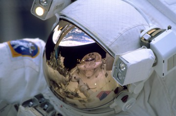 The entire forward portion of shuttle Discovery is reflected in the helmet visor of one of the STS-103 spacewalkers. Photo Credit: NASA