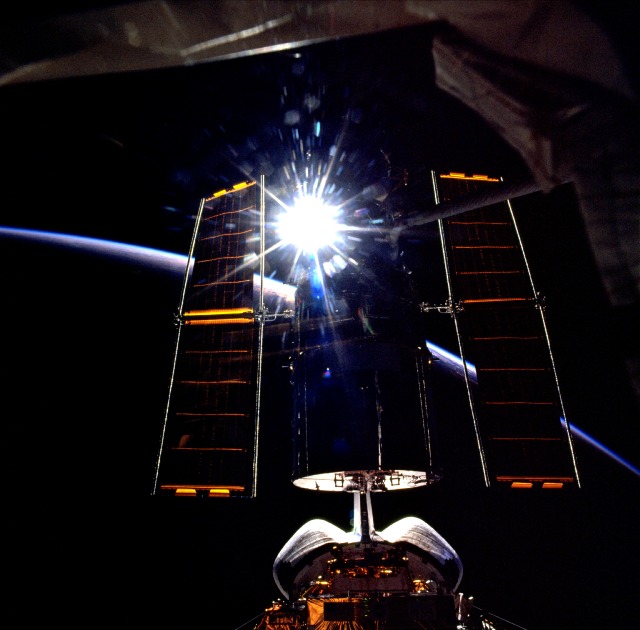 Orbital sunrise causes the solar arrays of the Hubble Space Telescope (HST) to glisten in this spectacular view from STS-103. Photo Credit: NASA