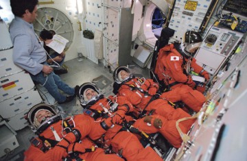For re-entry, Soichi Noguchi (background) would have occupied an upright seat in the middeck, with the returning Expedition 6 crew in recumbent seats. In this training image from November 2002, the Expedition 7 crew demonstrate the method. Photo Credit: NASA