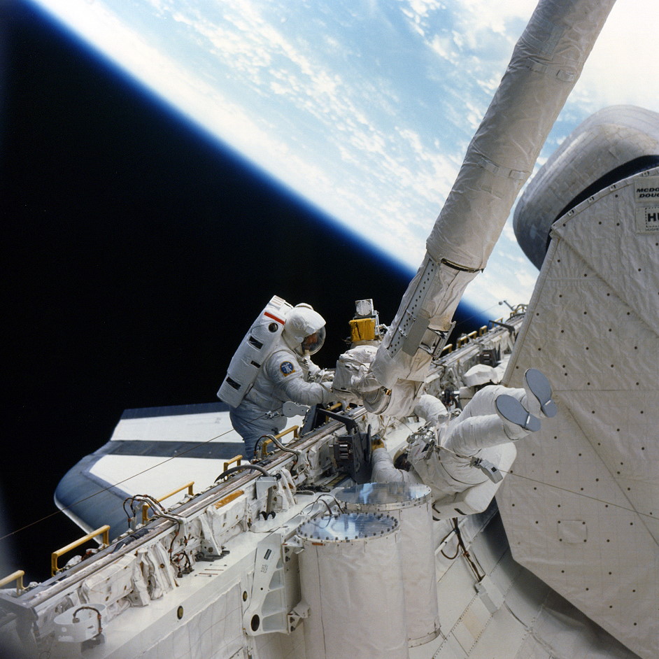 Spacewalkers Jeff Hoffman and Dave Griggs work to outfit a makeshift fly swatter onto the Remote Manipulator System (RMS) mechanical arm, in a fruitless attempt to activate Syncom 4-3's deploy switch. Photo Credit: NASA