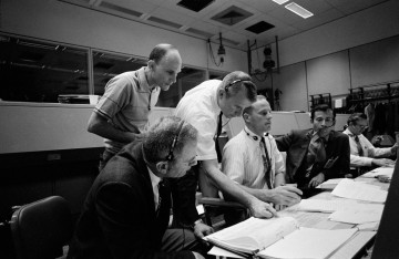Astronauts gather in Mission Control at the height of the crisis. Seated (from left) are Deke Slayton, Jack Lousma and John Young, with Ken Mattingly and Vance Brand standing. Photo Credit: NASA