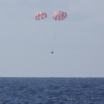 The CRS-6 spacecraft descends beneath three red-and-white parachutes, heading for a splashdown in the Pacific Ocean, after the longest-duration and longest-berthed Dragon mission to date. Photo Credit: SpaceX