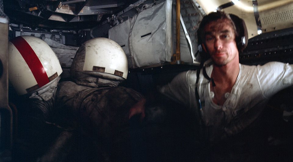 Covered in lunar grime, and clad only in his water-cooled underwear, Gene Cernan manages a grin for Jack Schmitt's camera, aboard the Lunar Module (LM) Challenger during the Apollo 17 mission in December 1972. The astronauts' space suits can be seen, stashed at the back of the cramped cabin. Above the helmets can be seen the hatch leading to the Command and Service Module (CSM) docking tunnel. Photo Credit: NASA, with thanks to Ed Hengeveld