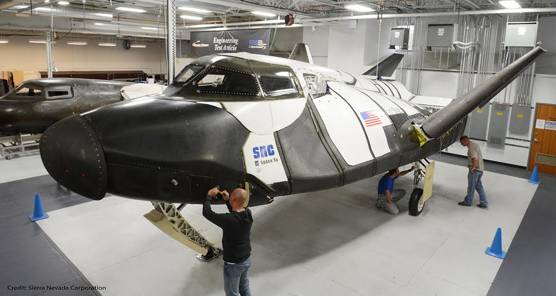 SNC technicians inspect the Dream Chaser engineering test article (ETA). A second advanced composite orbital vehicle is also being worked, which when tested will undergo a suborbital and orbital flight regimen, respectively. Flight testing is scheduled to resume sometime in 2016. Photo Credit: SNC