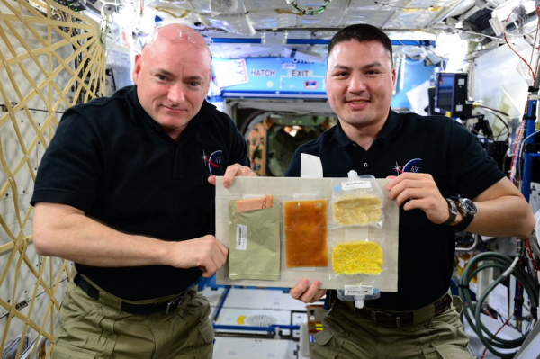 Expedition 45's Scott Kelly (left) and Kjell Lindgren display their Thanksgiving menu of turkey, candied yams, rehydratable corn and potatoes au gratin. Photo Credit: NASA