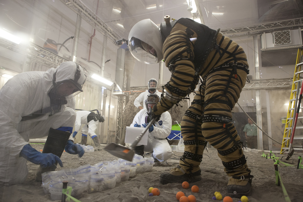 University researchers and engineers from University of North Dakota test their NDX-1 spacesuit inside the regolith bin at the Swamp Works facility at NASA KSC. Photo Credit: NASA 