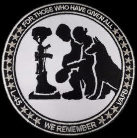 The overall mission patch for the launch shows the boots and automatic rifle of a fallen soldier, Marine or Airman with his dog and mourning teammates. Image Credit: NRO
