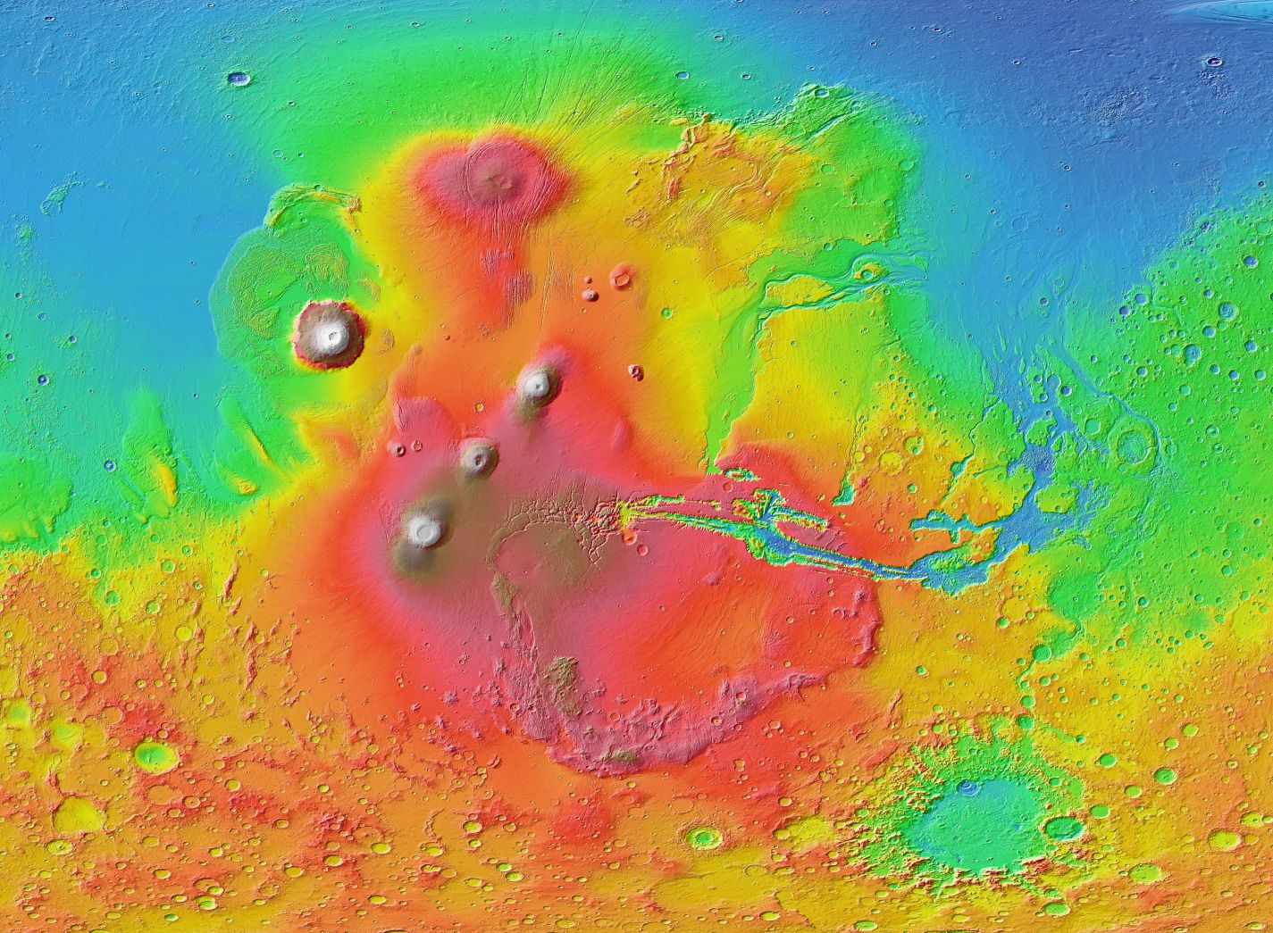A false-color relief map of the Tharsis region made from the Mars Orbiter Laser Altimeter onboard NASA's Mars Global Surveyor spacecraft. The Tharsis Montes are the three aligned volcanoes left of center. Olympus Mons sits off to the northwest. The oval feature in the north is Alba Mons. The canyon system Valles Marineris stretches eastward from Tharsis; from its vicinity, outflow channels that once carried floodwaters extend north. Image Credit/Caption: Wikipedia
