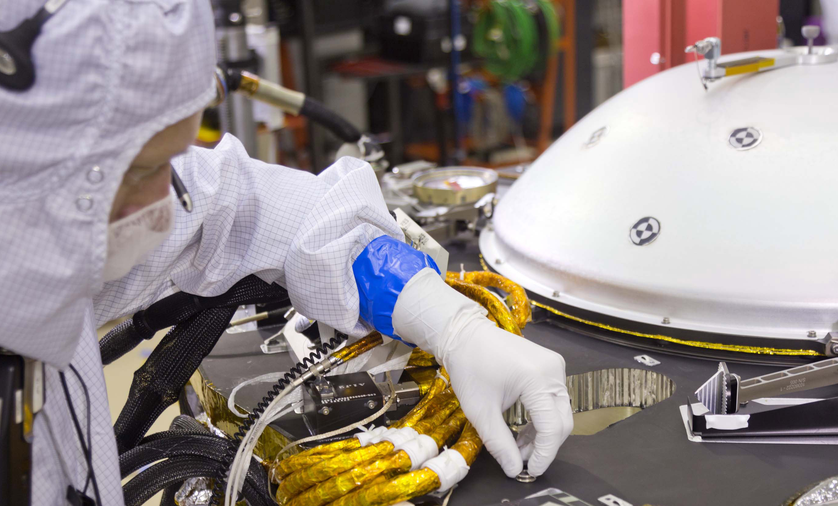 A spacecraft specialist in a clean room at Lockheed Martin Space Systems in Denver, where the InSight lander is being built, affixes a dime-size chip onto the lander deck in November 2015. This signature chip carries 826,923 names, submitted by the public online from all over the world. Photo Credit: NASA/JPL-Caltech/Lockheed Martin
