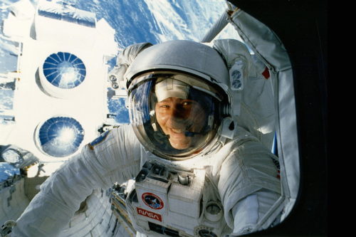 Astronaut Jerry Ross grins through shuttle Atlantis' aft flight deck windows, as the Compton Gamma Ray Observatory is readied for deployment in April 1991. Photo Credit: NASA, via Joachim Becker/SpaceFacts.de