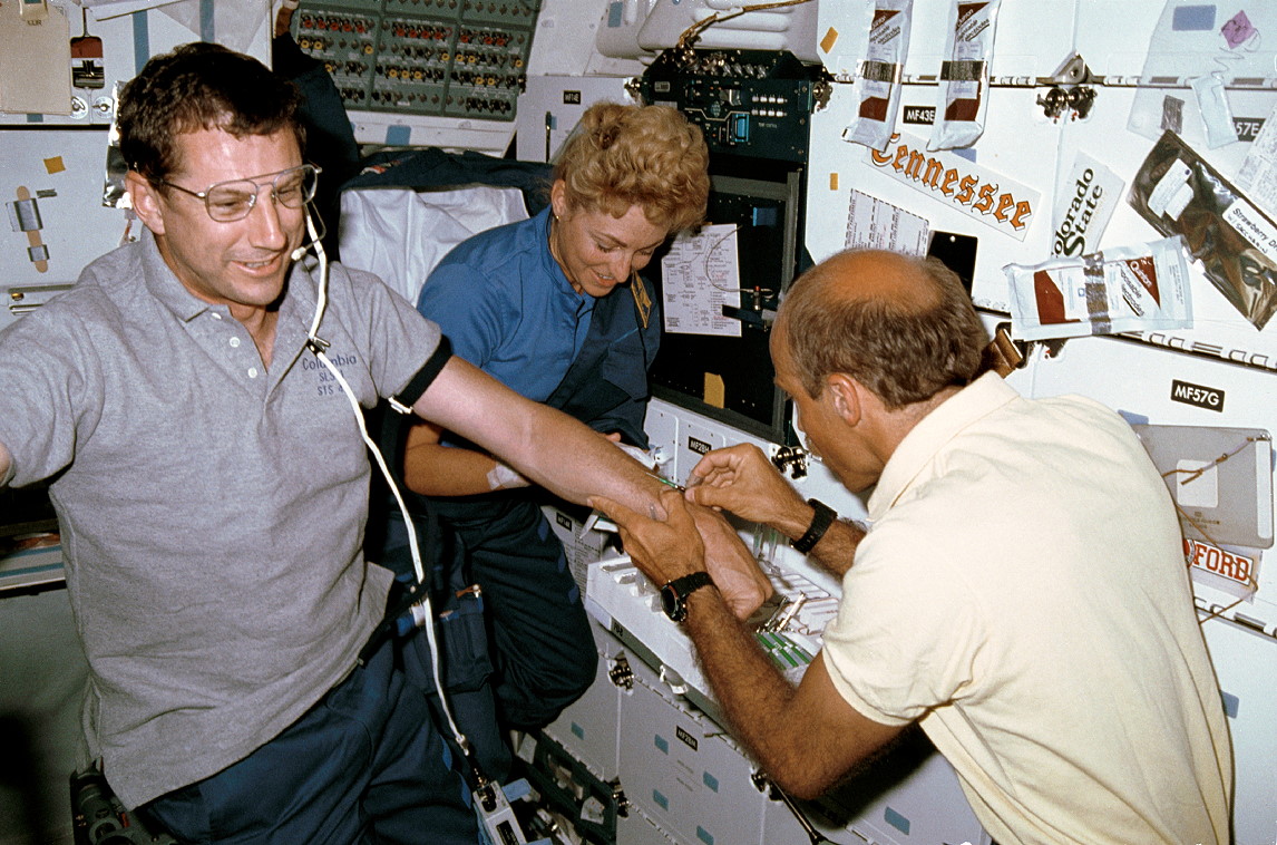Having ridden to orbit wearing a heart catheter, Drew Gaffney (left) offers his arm to Jim Bagian and Millie Hughes-Fulford for one of many blood draws. Photo Credit: NASA, via Joachim Becker/SpaceFacts.de