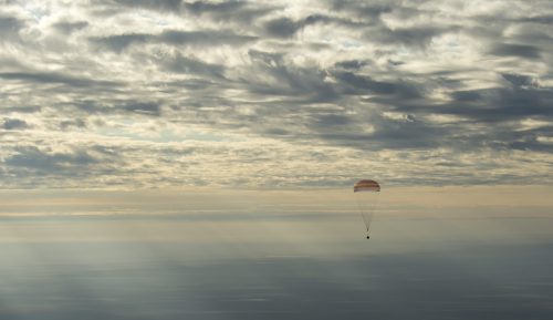 The Soyuz MS-01 spacecraft descends towards its landing site, beneath the large orange-and-white main parachute. Photo Credit: (NASA/Bill Ingalls)